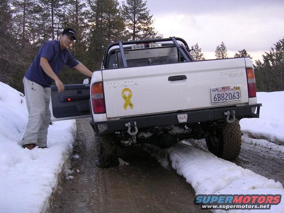 1999 Toyota Tacoma pickup truck with yellow ribbon sticker on tailgate, parked in snow. California license plate 6B82063