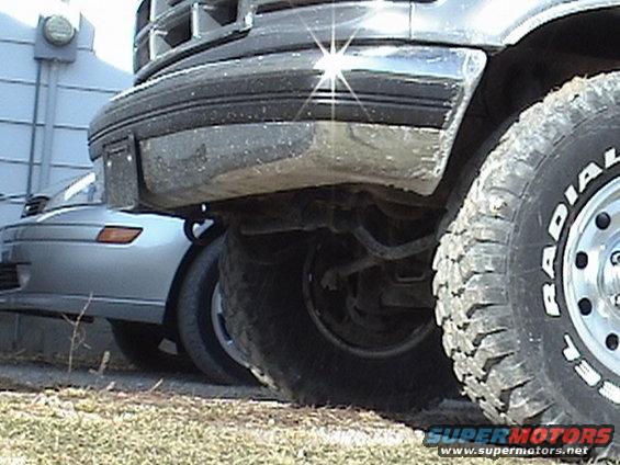 Truck front bumper and large tire, silver car in background