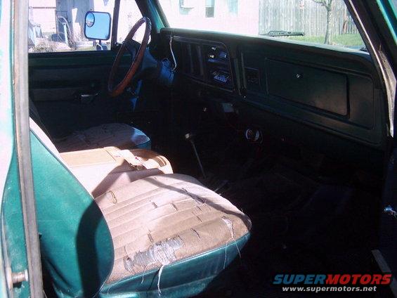 Interior shot of a green vehicle with worn seats, wood-rimmed steering wheel, and dashboard