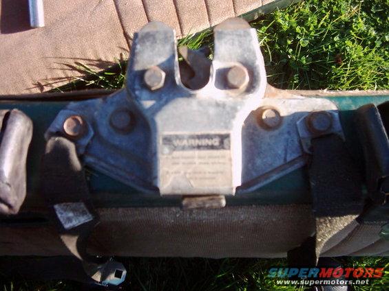 Close-up of a trailer hitch mechanism with a warning label. Straps are visible