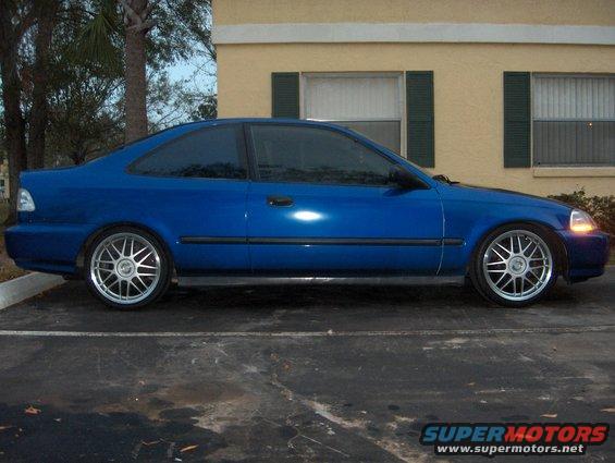Blue coupe with aftermarket wheels parked in front of a building