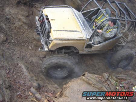 1989 Ford Bronco modified for off-roading, climbing a steep, muddy incline with a roll cage