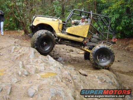 Yellow off-road vehicle with a roll cage going over rocks on a trail