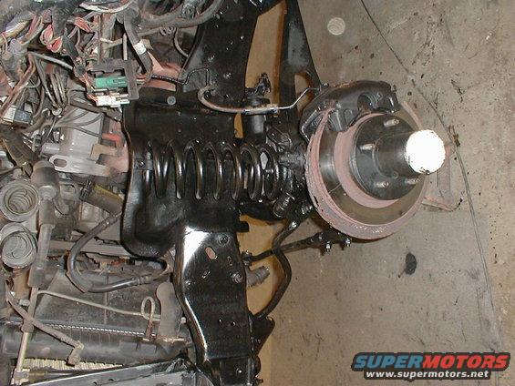 Close-up of vehicle front suspension, brake rotor, and engine wiring