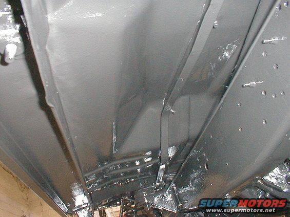 Underside view of vehicle frame rails and suspension components, painted gray