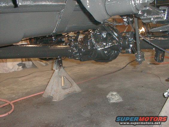 Underside of a vehicle on jack stands, showing the rear axle and suspension parts that have been painted black