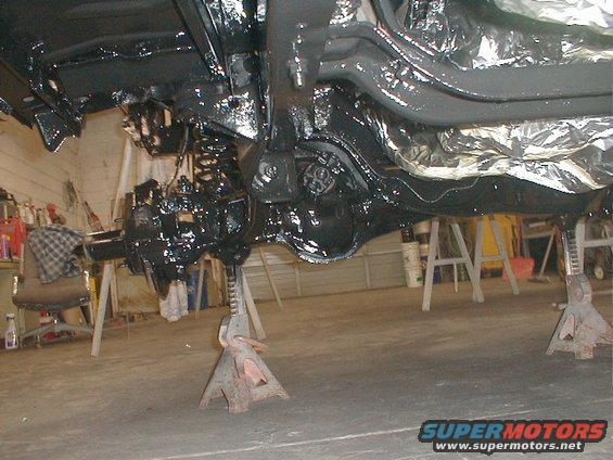 Undercarriage of a vehicle on jack stands, coated in black paint, with foil insulation visible