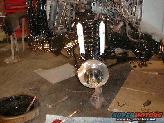 vehicle's front suspension and brake rotor assembly, with black painted frame components and white shock absorbers