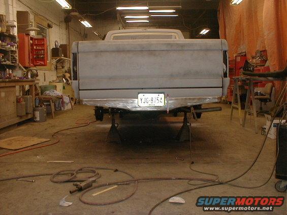 Gray 1987 Ford F-150 truck on jack stands in a garage, rear view