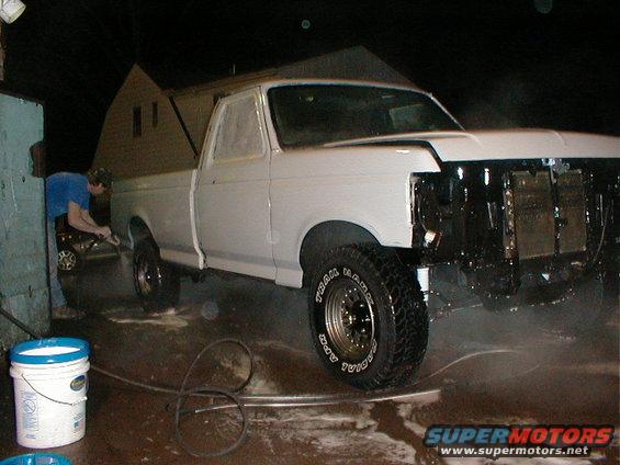 White pickup truck with front end removed, being washed by a person with a hose