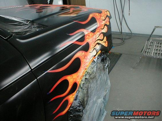 black car fender with orange and red flames painted on it, being worked on in a garage