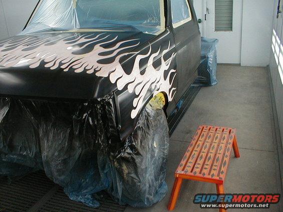 1991 Ford F-150 truck with custom flame paint, covered in plastic in a paint booth