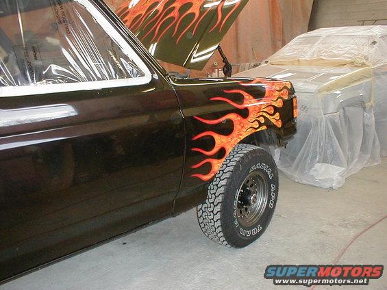 Truck with flame decals on fender and hood, another vehicle covered in plastic behind it