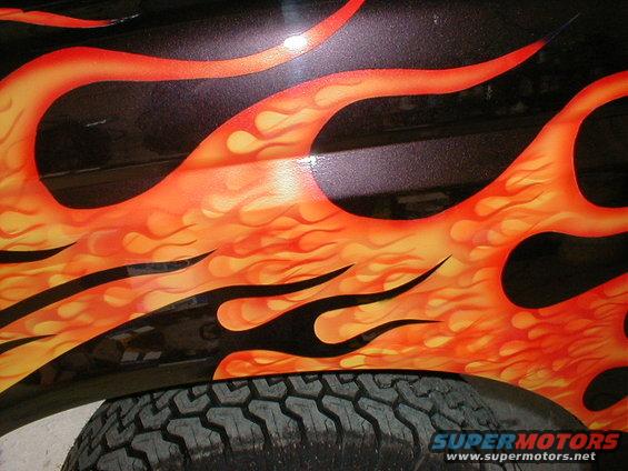 Close-up of orange and yellow flames painted on a black vehicle fender above a tire