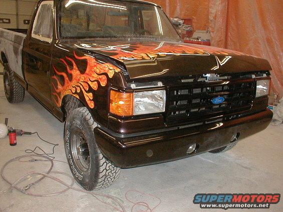 Dark brown Ford F-150 truck with orange and yellow flame graphics on the hood and fender, undergoing repairs
