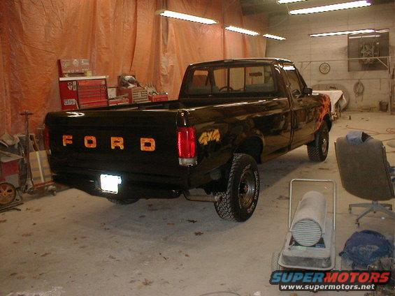 1991 Ford F-150 pickup truck, black with orange flames on the fender, parked in a garage