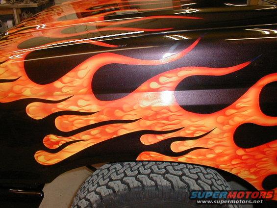 Close-up of a black truck fender with orange and yellow flame graphics and a tire visible