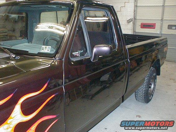 Side view of a dark-colored pickup truck with custom flame paint on the fender and door. It has a sticker on the driver's side window