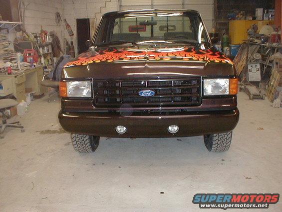 Brown 1991 Ford F-150 truck with orange and yellow flames on the hood, facing forward in a garage