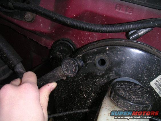 Hand holding a hose near brake booster and master cylinder in a red vehicle
