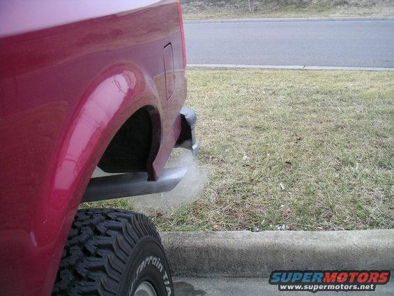 Red SUV's rear quarter panel, tire, and exhaust pipe emitting smoke. The body style suggests a 1992 model