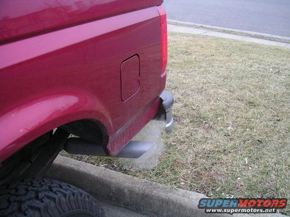 Red pickup truck's rear quarter panel, tire, and exhaust pipe emitting smoke