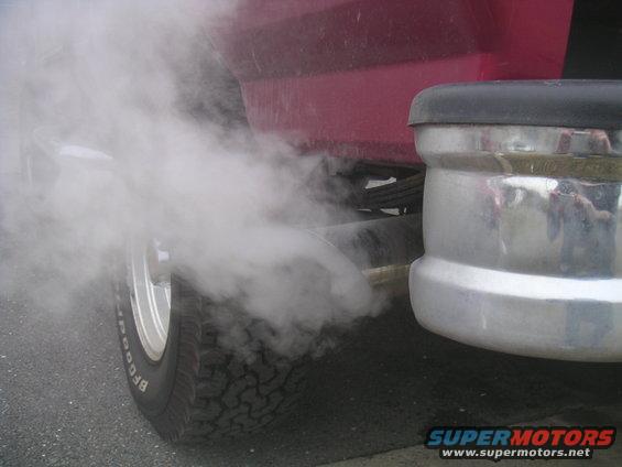 Exhaust smoke billowing from the tailpipe of a red vehicle, with a chrome bumper visible