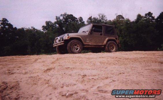 Brown Jeep Wrangler on sandy terrain with trees in background