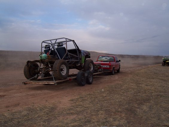 Buggy on trailer towed by red pickup, another green vehicle in distance