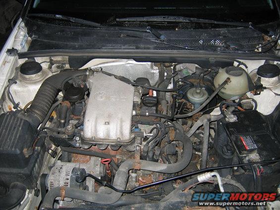 Engine bay of a Volkswagen, showing the engine, battery, and various hoses and wires