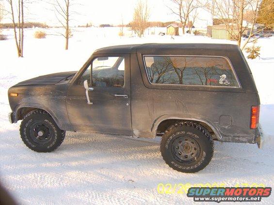 Side view of a dark-colored Ford Bronco parked in the snow. It has aftermarket wheels and tires