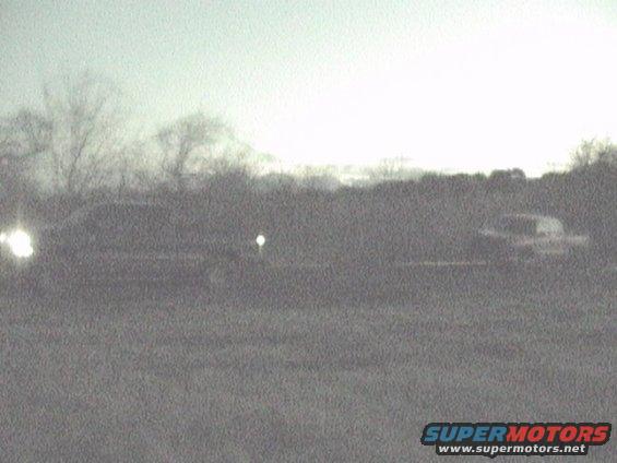 Two vehicles on a road, one with headlights on, at dusk