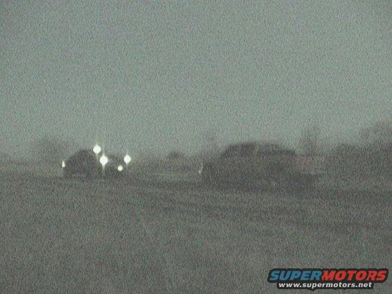 Two dark SUVs drive across a field in low light conditions, one with multiple headlights illuminated