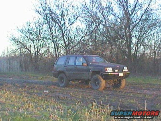 Dark colored Jeep Grand Cherokee with lifted suspension on a dirt road