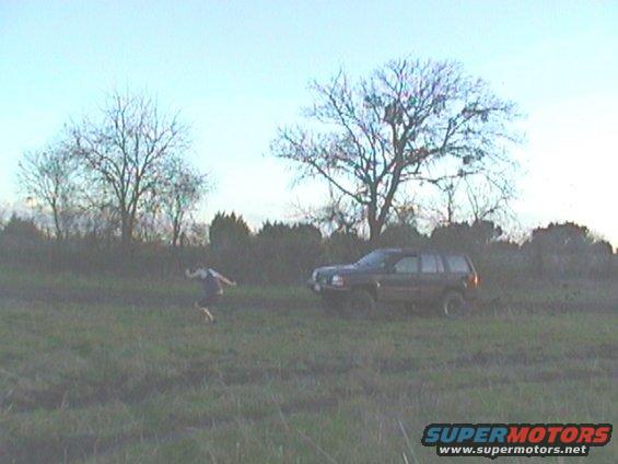 Dark colored Jeep Grand Cherokee parked in a grassy field with a person running nearby