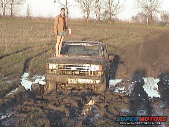 Mud-covered 1987 Ford F-Series truck stuck in mud with a woman standing on the hood