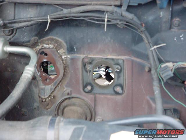 Firewall with two large holes, one with a brown gasket, near AC line and wiring harness