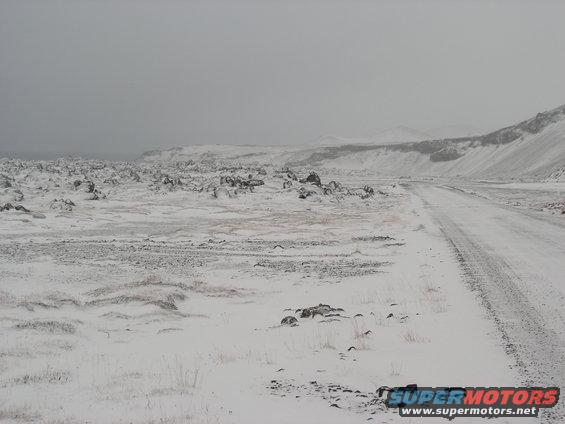 Snowy landscape with a dirt road winding through rocky terrain under an overcast sky