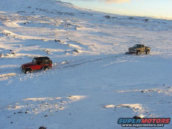 Red Jeep TJ being towed by pickup truck in snowy terrain