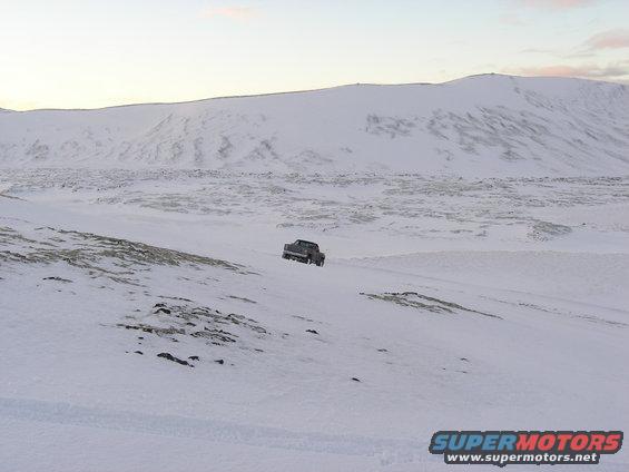 Dark pickup truck driving on a snowy, desolate landscape with mountains in the background