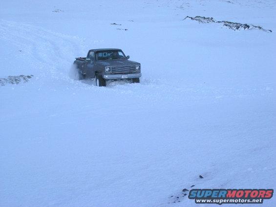 Dark pickup truck driving through snow, 1980s styling