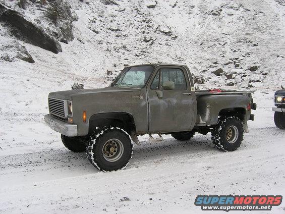 Old pickup truck with large tires on a snowy road, another vehicle visible to the right