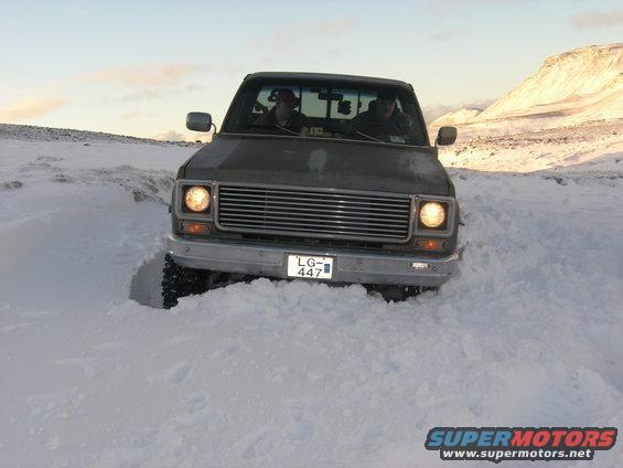 Pickup truck driving through deep snow, two people inside
