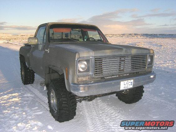 Gray pickup truck with large tires in snow, front grille visible