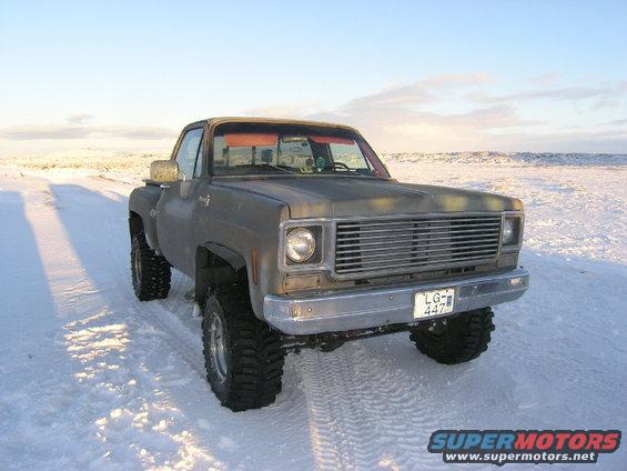 Lifted pickup truck with large tires parked in a snowy field. License plate reads LG-447