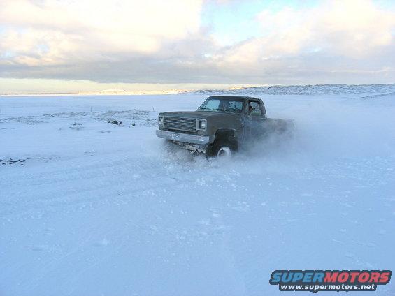 Pickup truck drifting in a snowy field, kicking up snow