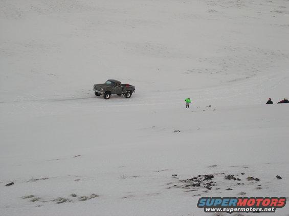 Gray pickup truck driving on a snowy field with a person in a green jacket nearby