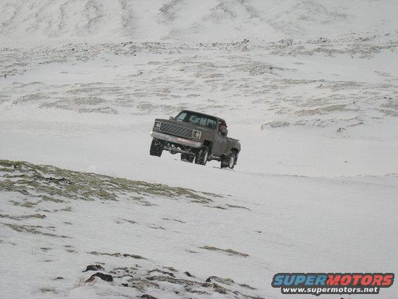 Brown pickup truck with lifted suspension driving on a snow-covered hill