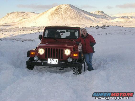 Red 2001 Jeep TJ in snow, front view, with a woman standing next to it