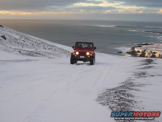 Red Jeep Wrangler driving on a snowy hill overlooking the ocean